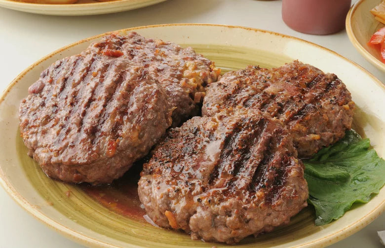 Four grilled boere burger patties on a plate with a side of lettuce.