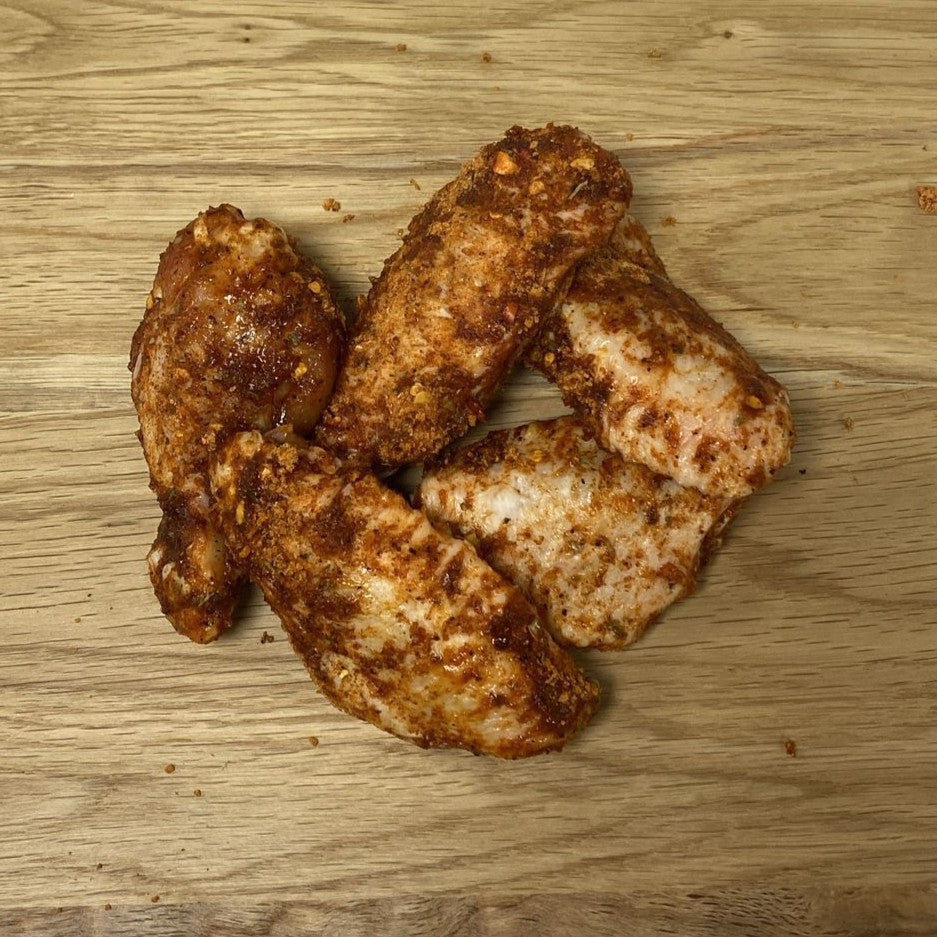 Several chicken wings seasoned with peri peri sauce from Biltong Direct on a wooden surface.