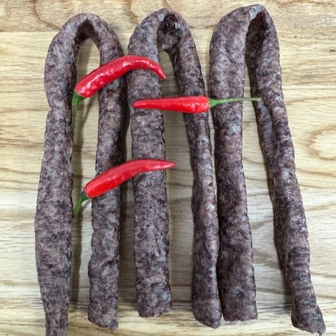A selection of Chilli Droewors from Biltong Direct, a traditional South African air-dried sausages, with a bold chilli kick, displayed on a wooden surface, garnished with red chili peppers.