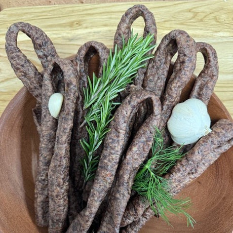 A bowl containing air-dried beef sausages (Droewors) from Biltong Direct with a garlic twist, garnished with dill and garlic cloves.