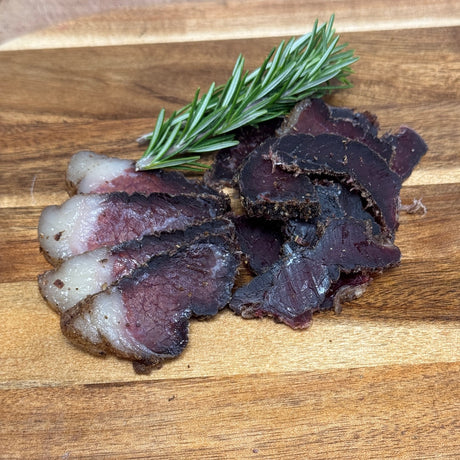 Sliced biltong from Biltong Direct on a wooden board with a sprig of rosemary.