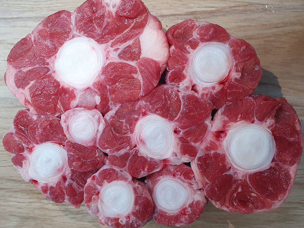 A tray of fresh oxtail pieces from Biltong Direct, showing the bone and the meat attached to it, on a wooden surface.