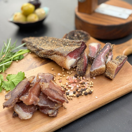 Original beef biltong both chucks and slices from Biltong Direct on a wooden cutting board with olives in the background