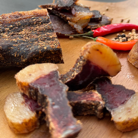 Dried chilli biltong chunk and slices from Biltong Direct on a wooden board with red peppers and spices