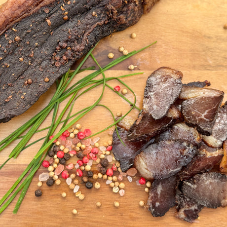 Dried trekkers beef biltong a whole piece and slices from Biltong Direct with chives and peppercorns on a wooden board