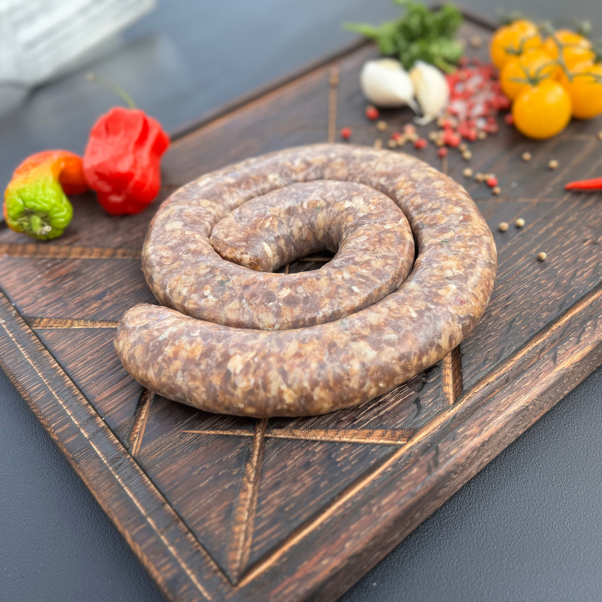 Coiled chakalaka boerewors sausage from Biltong Direct on a wooden cutting board with peppers and tomatoes in the background