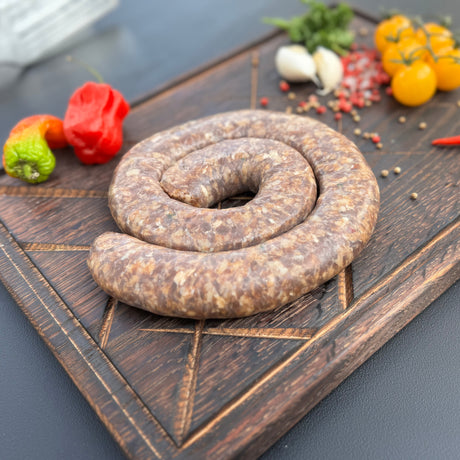 Coiled chakalaka boerewors sausage from Biltong Direct on a wooden cutting board with peppers and tomatoes in the background