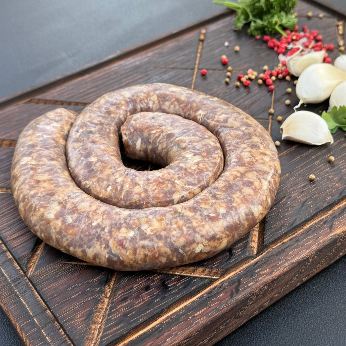 Coiled raw garlic boerewors sausage from Biltong Direct on a wooden surface with Garlic, herbs and spices.