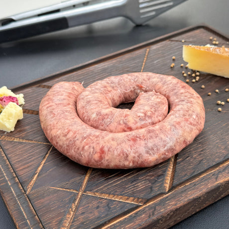Coil of raw Kaas (cheese) boerewors sausage from Biltong Direct on a wooden cutting board with a block of cheese in the background