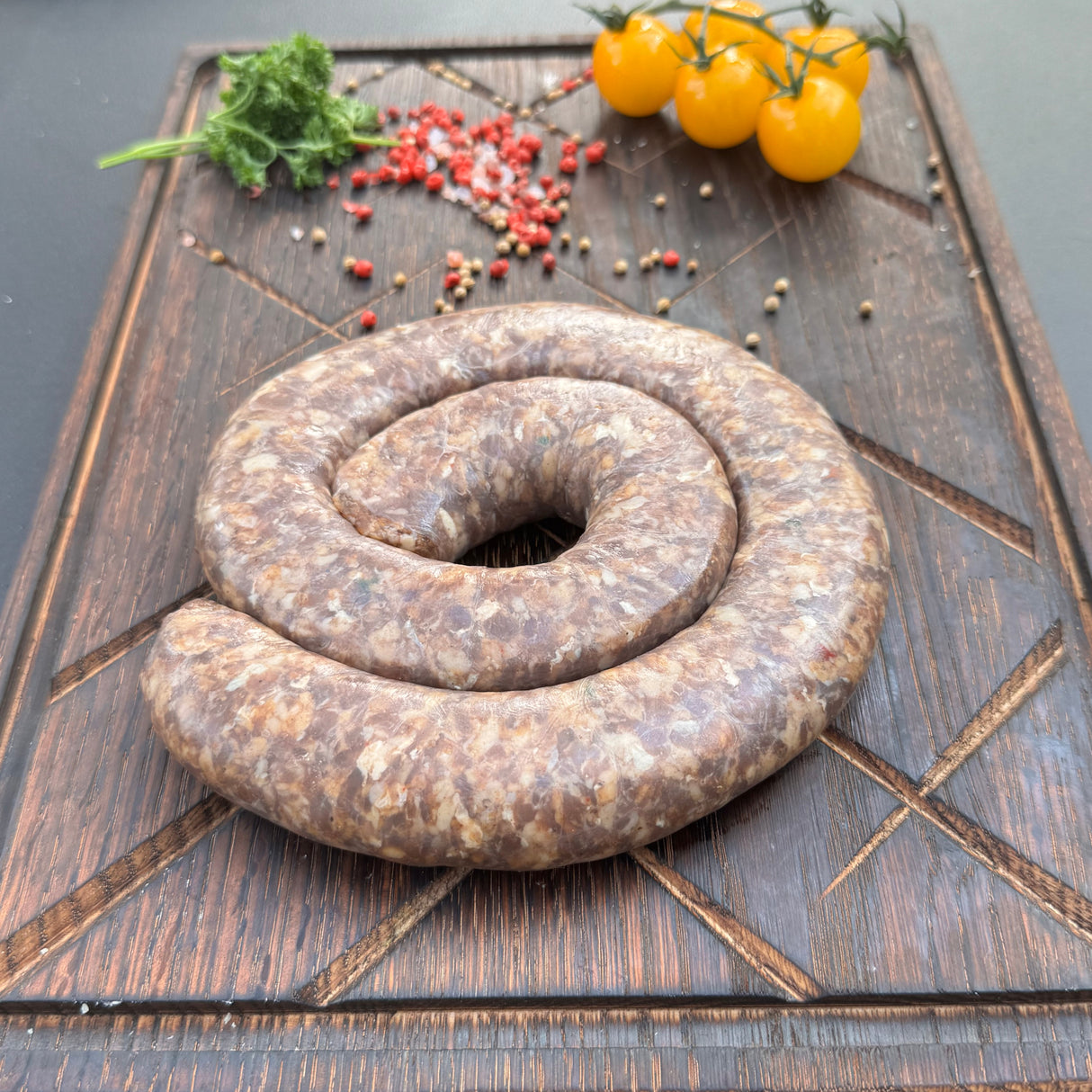 Coiled raw Traditional boerewors sausage from Biltong Direct on a wooden cutting board with vegetables.