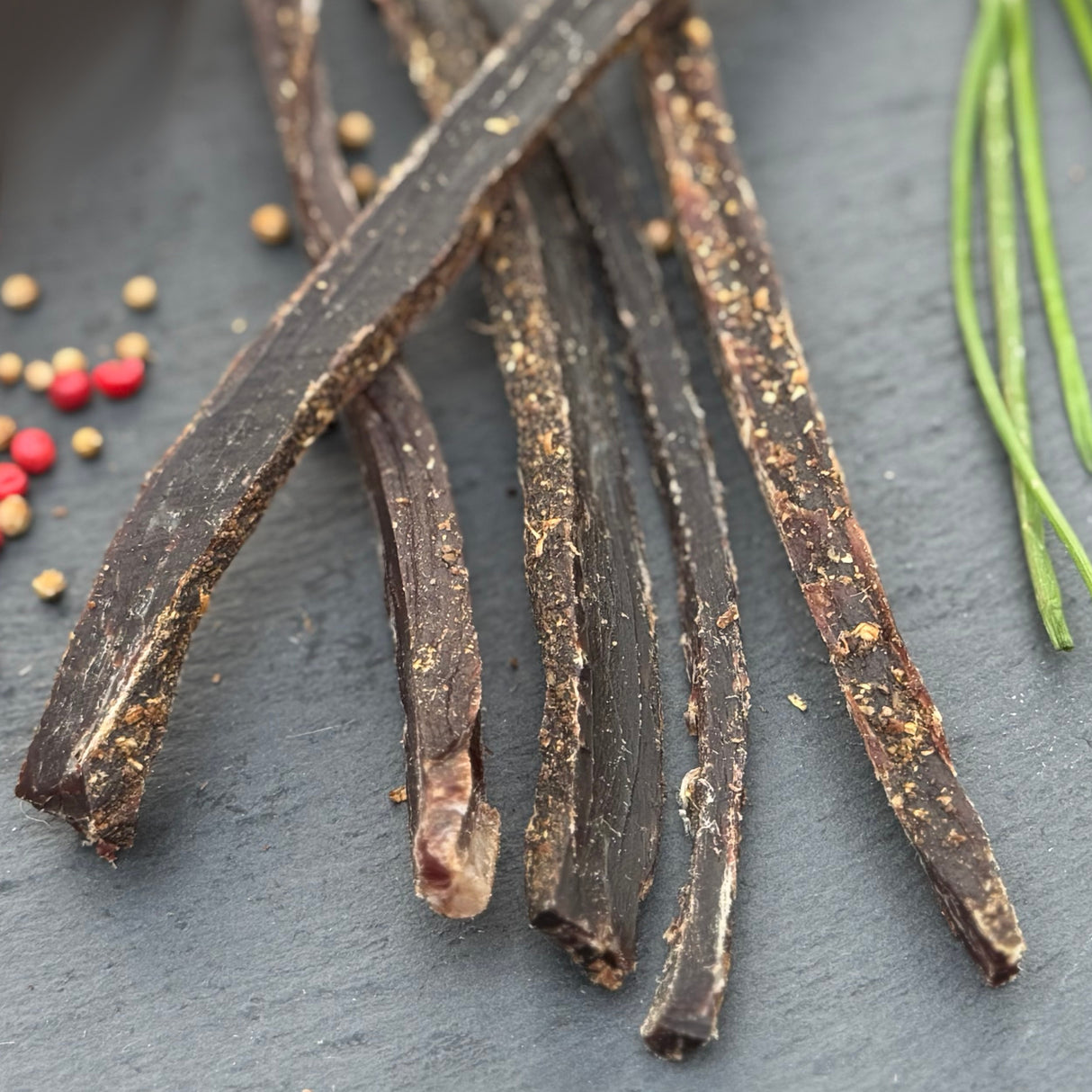 Dried beef biltong from Biltong Direct on a dark surface with small red and yellow seeds.