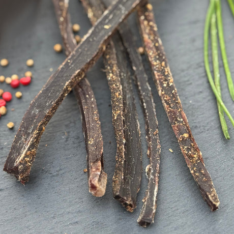 Dried beef biltong from Biltong Direct on a dark surface with small red and yellow seeds.