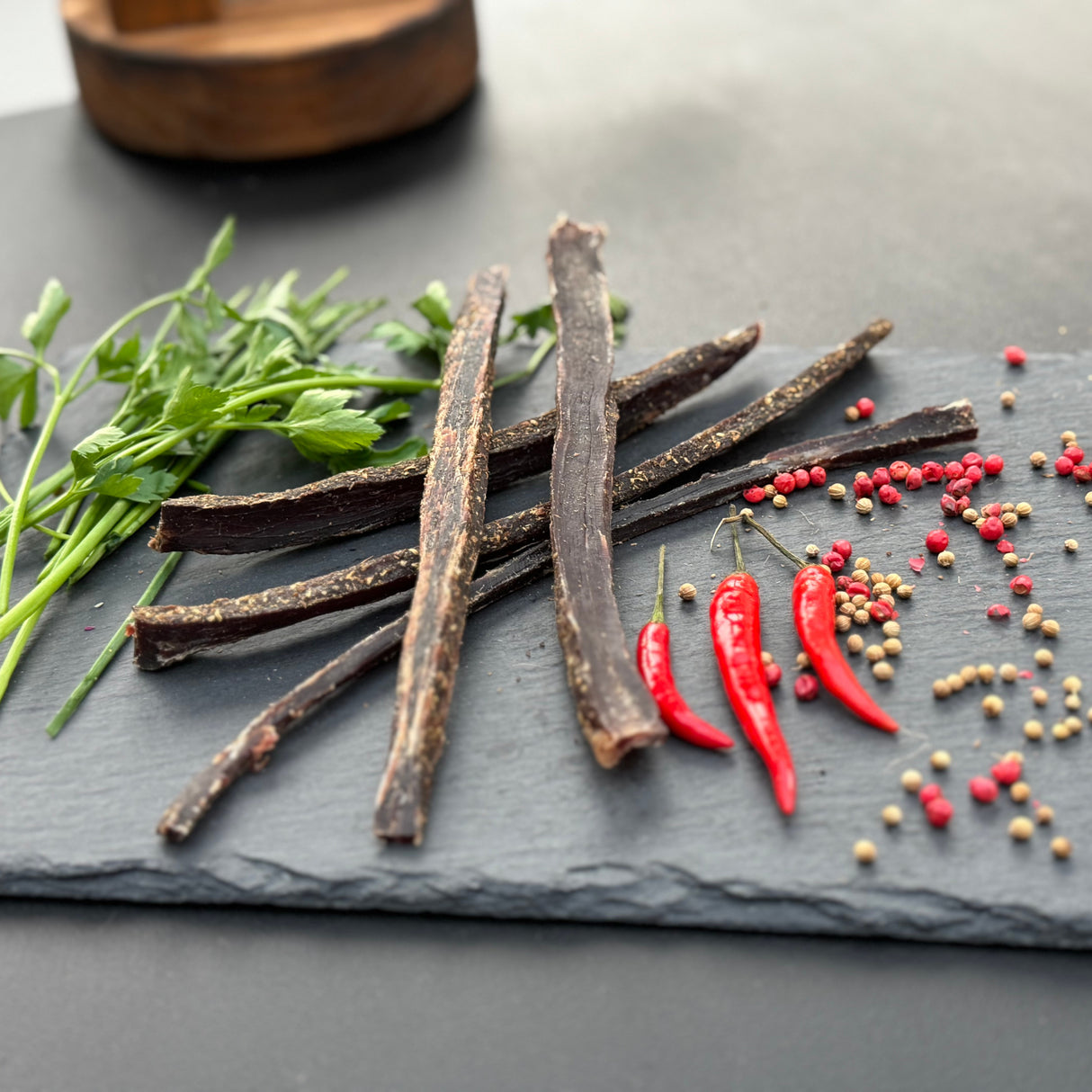 Dried beef biltong sticks from Biltong Direct a slate board with red peppers and spices