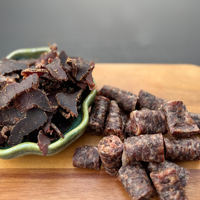 Dried beef biltong and droewors pieces on a wooden board from Biltong Direct