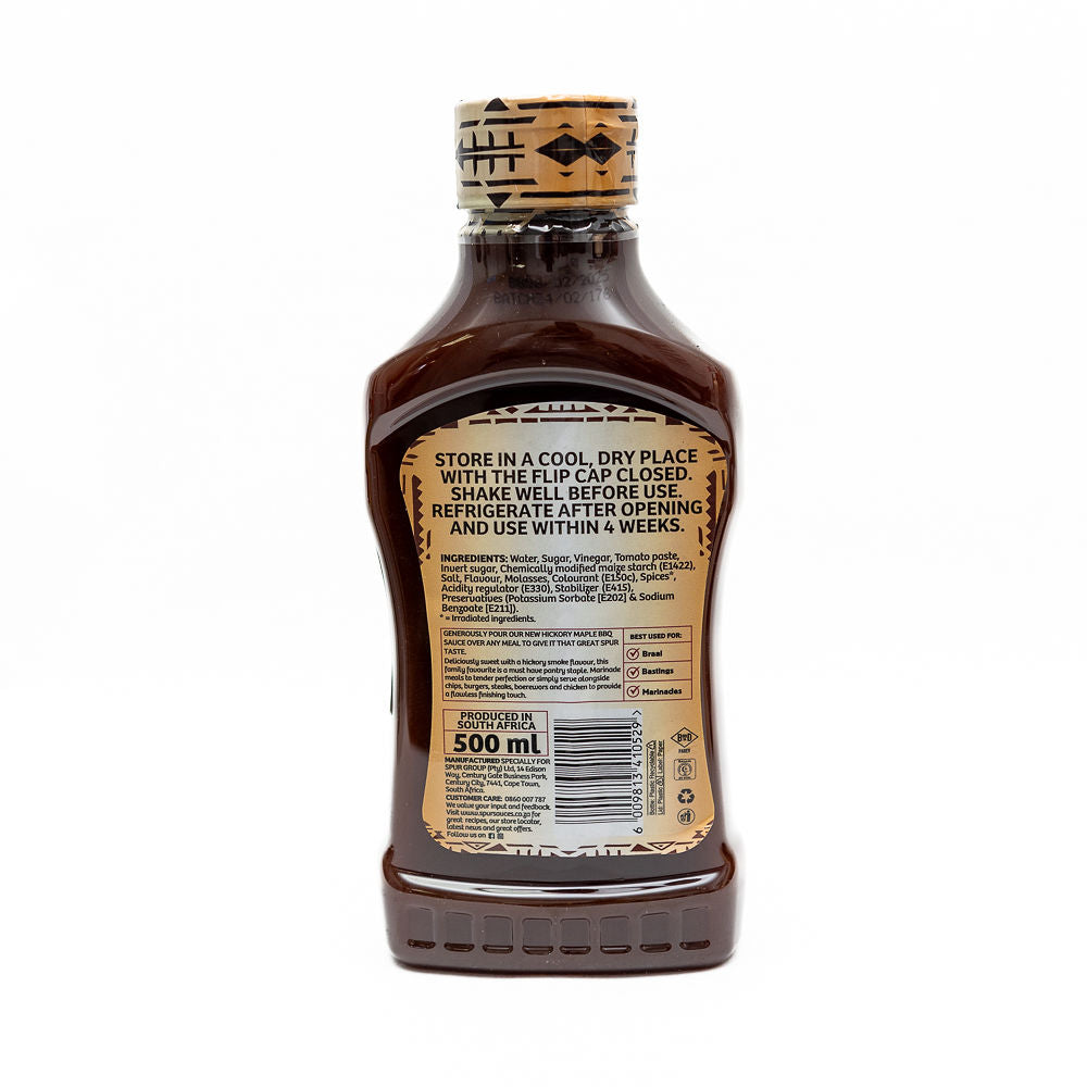 The back of the bottle of Spur Hickory Maple BBQ Sauce from Biltong Direct with a label showing the brand logo, the type of sauce, and a description of 'All new'. The sauce is in a clear bottle with a cork top.