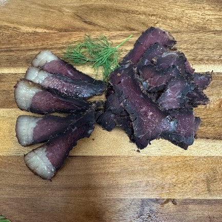 Slices of biltong from Biltong Direct on a wooden board with a sprig of dill.