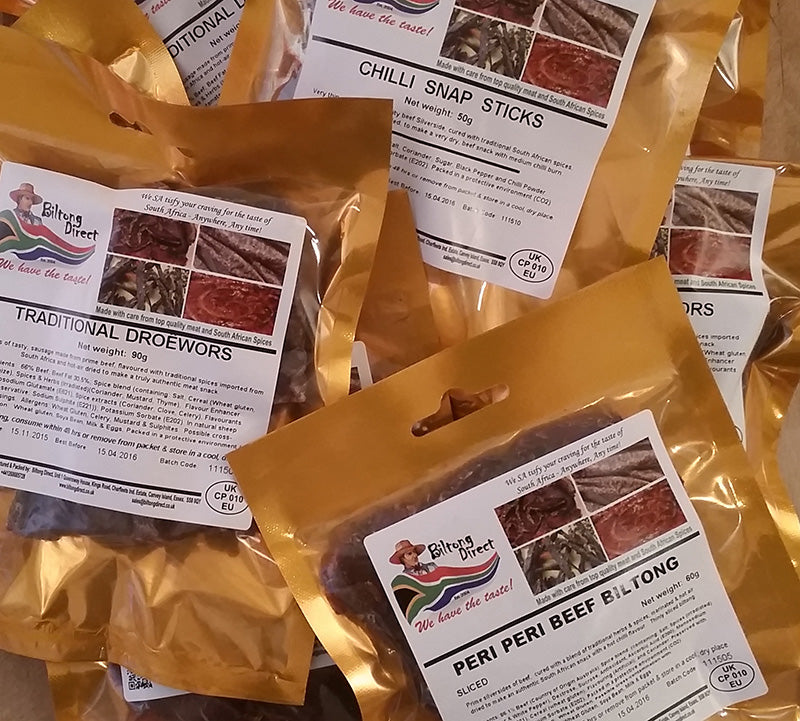 Multiple packets of Biltong Direct products including Traditional Biltong, Droewors, Snap Sticks, and Beef Crisps in both regular and chilli flavors, sealed in gold-colored packaging with labels showing the product name and flavor.
