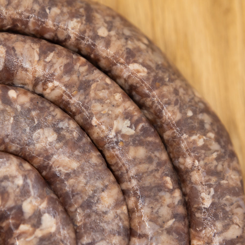 A close up of a large coil of traditional Mini Boerewors sausage from Biltong Direct laid out on a wooden surface.