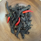 A wooden plate containing snap sticks, which are crispy beef biltong strips from Biltong Direct, garnished with red chili peppers.