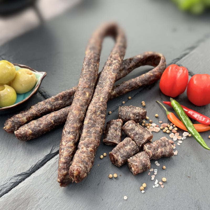 Droewors or drywors, a dried sausage from Biltong Direct on a dark surface with peppers and olives
