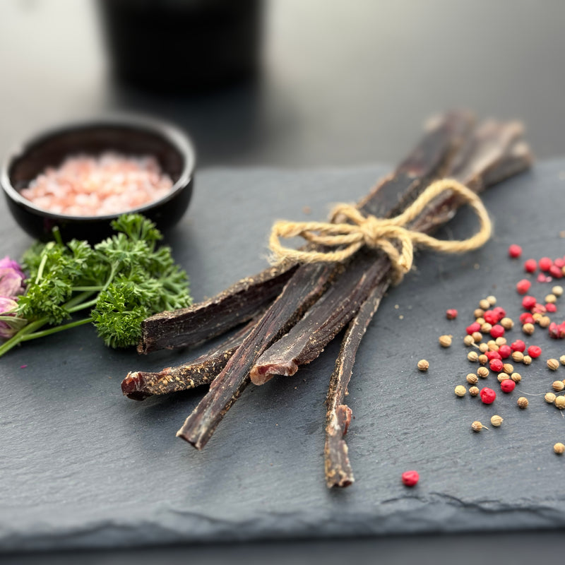 Biltong chews from Biltong Direct tied with twine on a slate surface with herbs and spices.