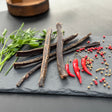 Dried beef biltong sticks from Biltong Direct a slate board with red peppers and spices
