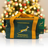 Green and yellow bag with 'World Champions' and 'Springboks' text against a blurred festive background