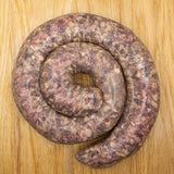 A coil of raw garlic Boerewors sausage from Biltong Direct laid out on a wooden surface.